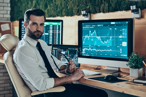 Junger Trader handelt an drei Bildschirmen. Professeionelle Handelsplattform, übersichtlich und benutzerfreundlich. Erfahrener Trader mit eigener Strategie die zum Erfolg führt. Handel mit CFDs, ETFs, Aktien, Fonds, Kryptowährungen, Forex und vieles mehr. Optimaler Arbeitsplatz. Optimistisch bleiben und Chancen erkennen. Chart- und Fundamentalanalyse einsetzen um besten Zeitpunkt für Trades auszumachen.
